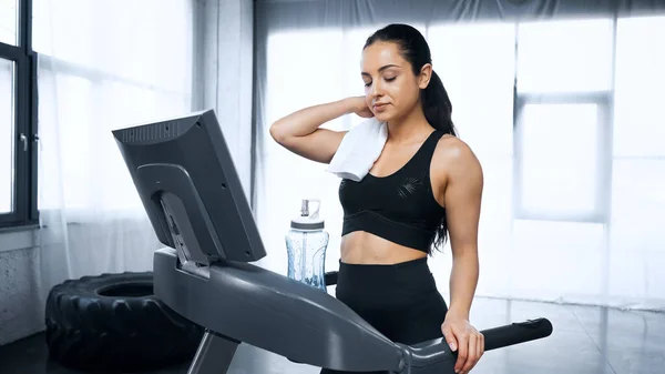 Sportswoman with towel walking on treadmill near sports bottle with water in gym — Stock Photo