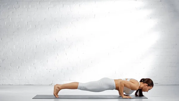 Vista lateral de la mujer que hace la pose del personal de cuatro extremidades en la estera del yoga - foto de stock