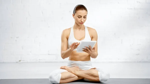 Jeune femme utilisant une tablette numérique tout en étant assis dans la pose du lotus — Photo de stock