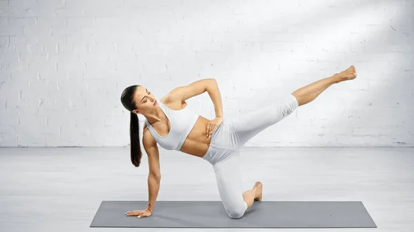 Frau in Sportbekleidung mit Hand an der Hüfte praktiziert Yoga zu Hause — Stockfoto