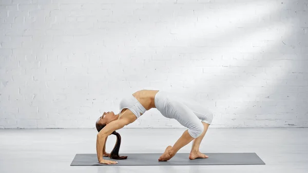 Seitenansicht einer hübschen Frau, die sich auf Yogamatte zurückbeugt — Stockfoto