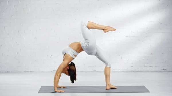 Vista lateral de la mujer descalza en pose de arco hacia arriba en la esterilla de yoga en casa - foto de stock