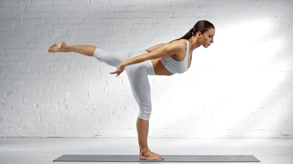 Vista lateral de mujer descalza en pose guerrera practicando yoga en casa - foto de stock