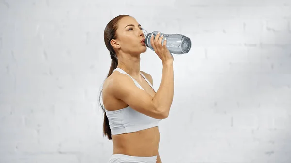 Sportswoman drinking water from sports bottle at home — Stock Photo