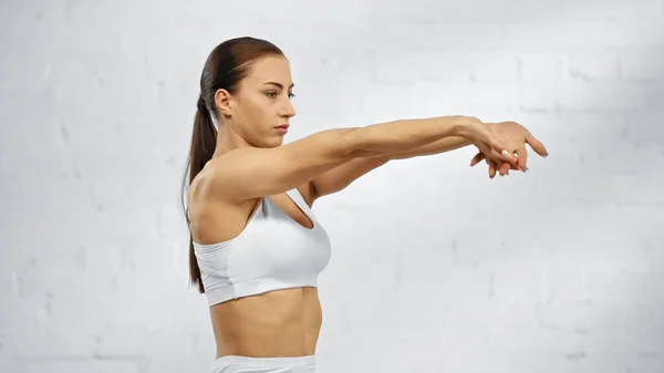 Brunette sportswoman stretching arms at home — Stock Photo