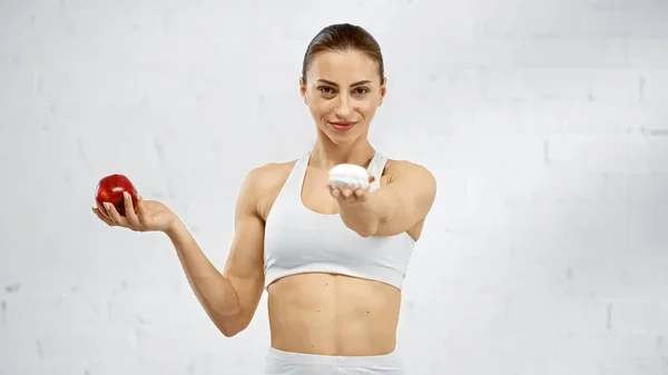 Smiling sportswoman holding blurred marshmallow and apple — Stock Photo