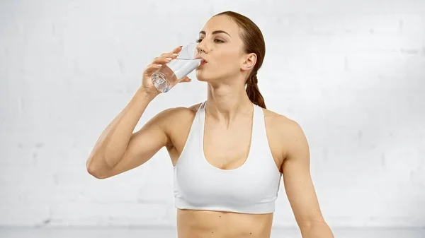 Sportswoman drinking water near white wall — Stock Photo