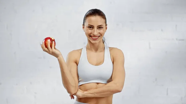 Positive sportswoman holding apple and looking at camera — Stock Photo