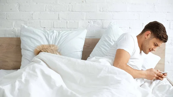 Uomo barare mentre sms su smartphone vicino donna dormire in camera da letto — Foto stock