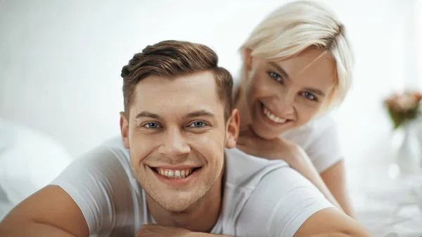 Mulher desfocada e feliz sorrindo enquanto deitado na cama com namorado — Fotografia de Stock