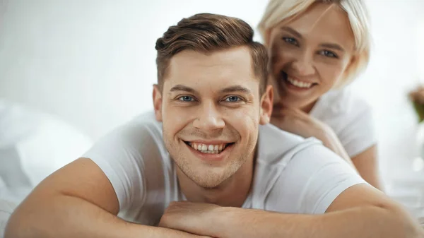Blurred and cheerful woman smiling while lying on bed with boyfriend — Stock Photo