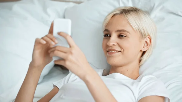 Mujer joven feliz mensajes de texto en el teléfono inteligente en el dormitorio - foto de stock