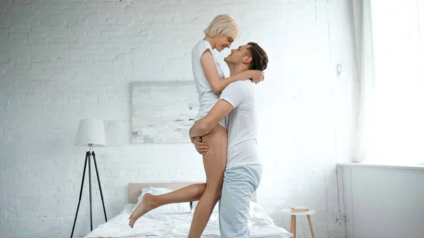 Side view of cheerful man holding in arms blonde woman in bedroom — Stock Photo