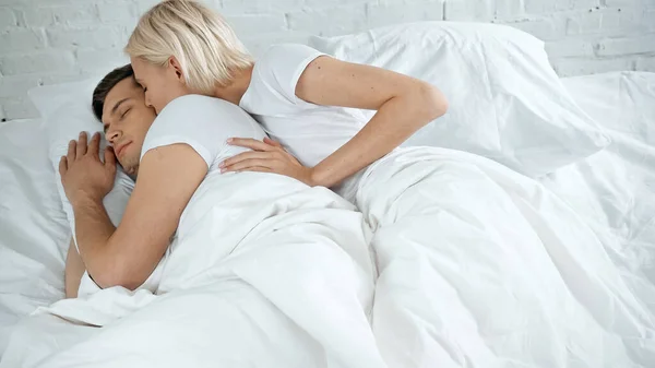Joven mujer besos joven hombre durmiendo en cama - foto de stock