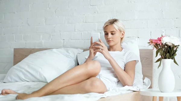 Mujer rubia joven usando smartphone en la cama - foto de stock