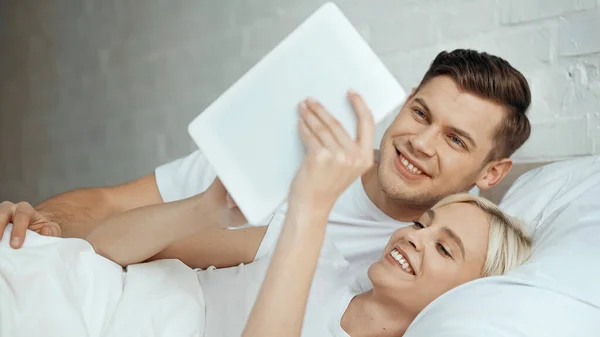 Mujer feliz sosteniendo la tableta digital y tomando selfie con el hombre - foto de stock