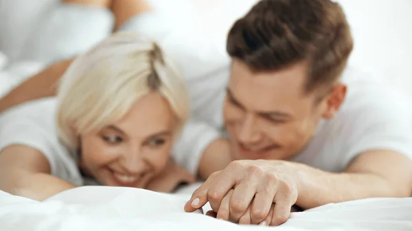 Verschwommene junge Mann und Frau Händchen haltend und lächelnd im Bett — Stockfoto