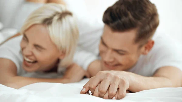Размытые молодая женщина и мужчина, держащиеся за руки и смеющиеся в постели — стоковое фото