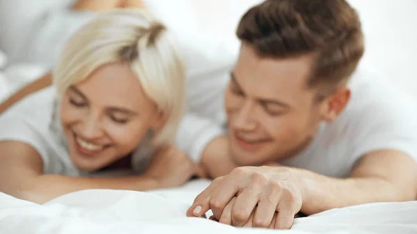 Mujer feliz borrosa y hombre tomados de la mano y sonriendo en la cama - foto de stock