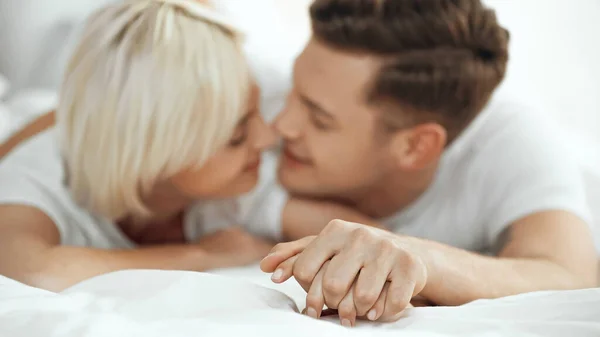 Mujer borrosa y hombre tomados de la mano y sonriendo en la cama - foto de stock