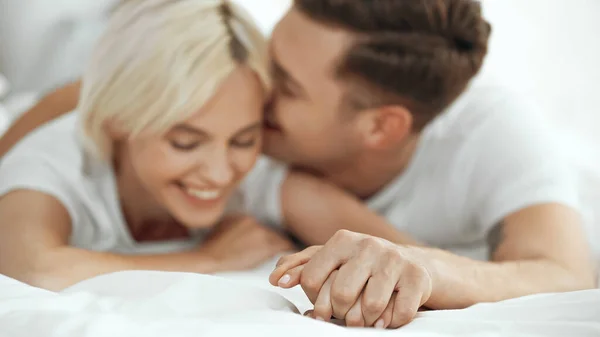 Размытые молодая женщина и мужчина, держащиеся за руки и улыбающиеся в постели — стоковое фото