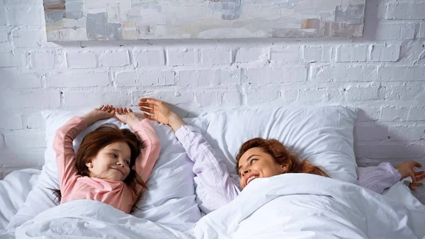 Criança sorridente e mãe deitada na cama de manhã — Fotografia de Stock