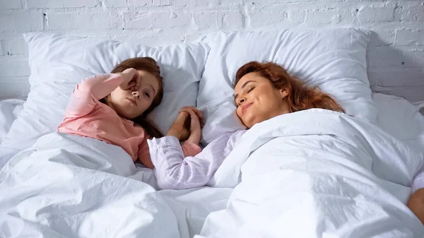 Sonriente madre y niño tomados de la mano en la cama - foto de stock