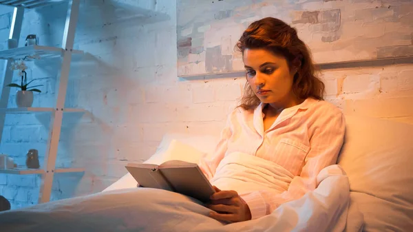 Woman in pajamas reading book on bed — Stock Photo