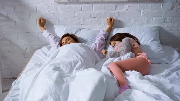 Frau streckt sich morgens neben schlafendem Kind auf Bett — Stockfoto