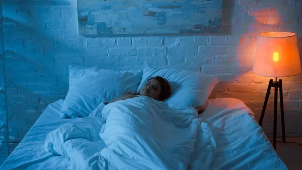 Woman sleeping on bed near floor lamp in bedroom — Stock Photo