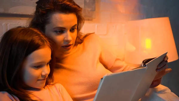 Mother and preteen girl reading blurred book in bedroom — Stock Photo