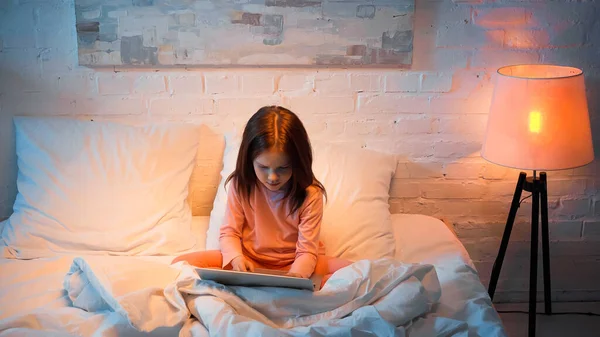 Kind benutzt Laptop auf Bett neben Stehlampe im Schlafzimmer — Stockfoto