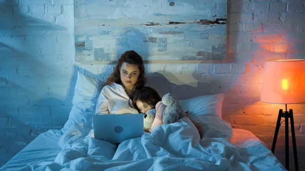 Teleworker usando laptop perto de criança dormindo na cama — Fotografia de Stock