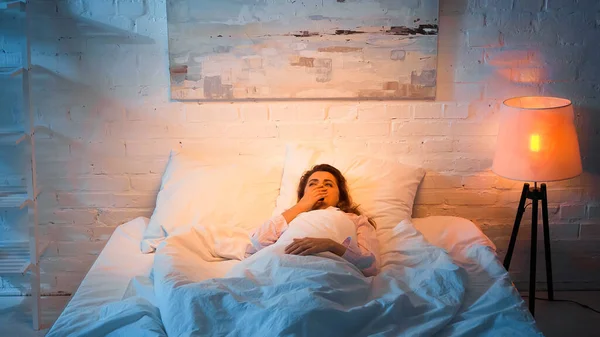 Femme bâillant alors qu'elle était allongée sur son lit le soir — Photo de stock