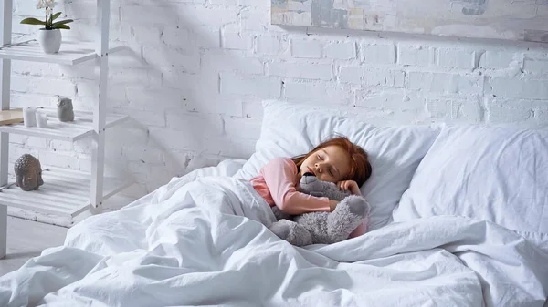 Child hugging teddy bear while sleeping on bed — Stock Photo