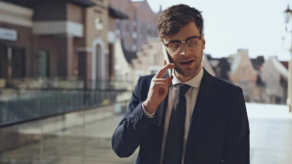 Happy businessman in glasses talking on smartphone in modern shopping center — Stock Photo