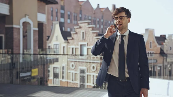 Happy businessman in glasses talking on smartphone in modern shopping center — Photo de stock