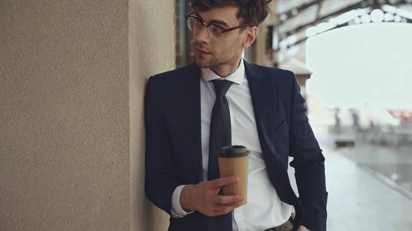 Симпатичный бизнесмен в очках и костюме держит кофе, чтобы пойти в торговый центр — стоковое фото