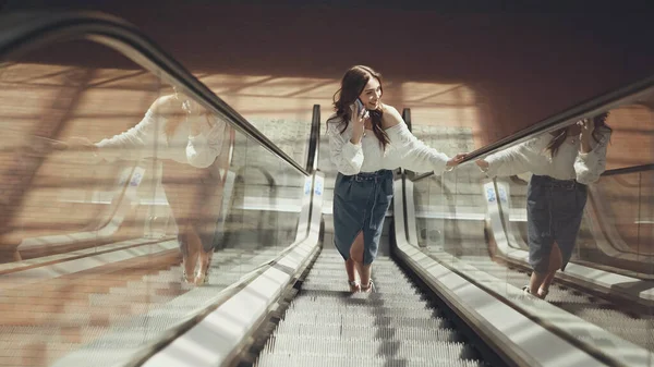 Счастливая молодая женщина с помощью смартфона на эскалаторе — стоковое фото