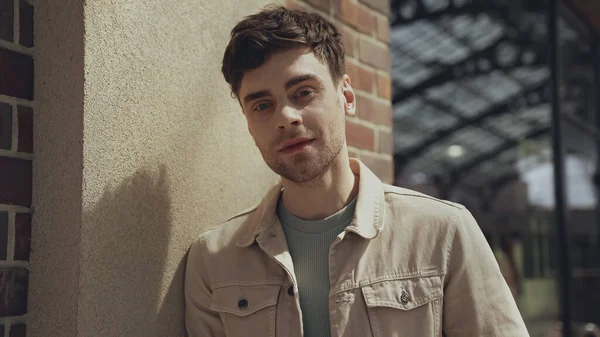 Good-looking man in beige jacket looking at camera in shopping mall — Photo de stock