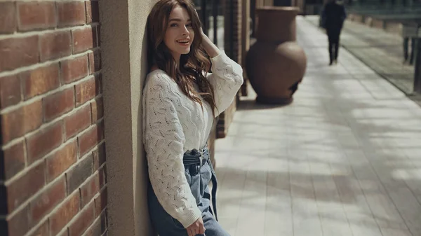 Positive young woman looking at camera near building of shopping mall — Stock Photo