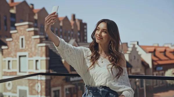 Lächelnde junge Frau macht Selfie in der Nähe verschwommener Gebäude — Stockfoto