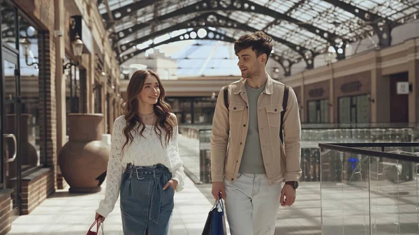 Весёлые мужчина и женщина ходят с сумками в торговом центре — стоковое фото
