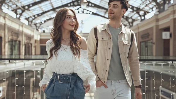 Happy woman and man posing with hands in pockets in shopping mall — Stock Photo