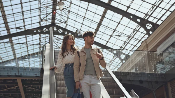 Happy man and woman standing on escalator in shopping mall — Stock Photo