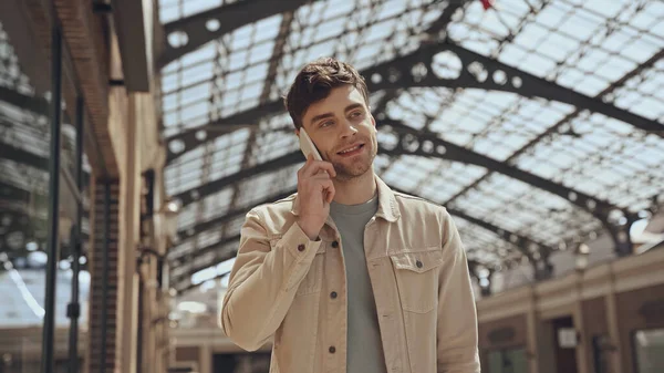 Улыбающийся мужчина разговаривает по смартфону в торговом центре — стоковое фото