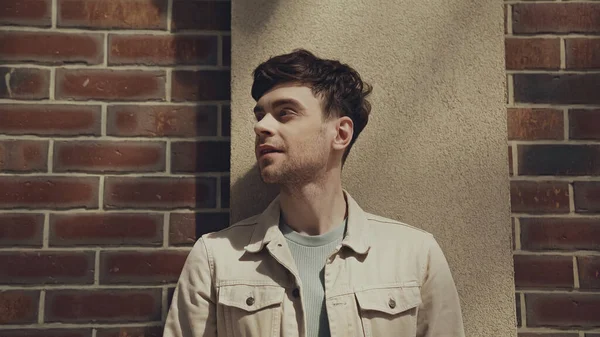 Smiling man in beige jacket looking away near building outside — Photo de stock