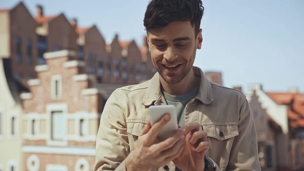 Щасливий чоловік використовує смартфон із розмитою будівлею на фоні — стокове фото