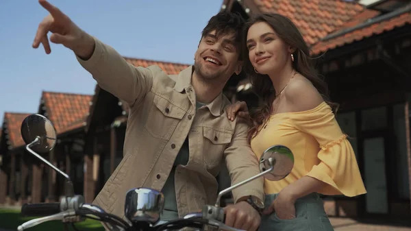 Happy man pointing with finger while sitting on motorcycle with young woman — Stock Photo