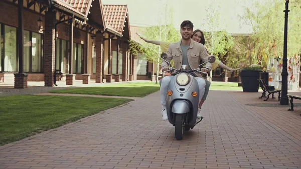 Радостный мужчина и счастливая женщина с протянутыми руками верхом на мотоцикле по улице — стоковое фото